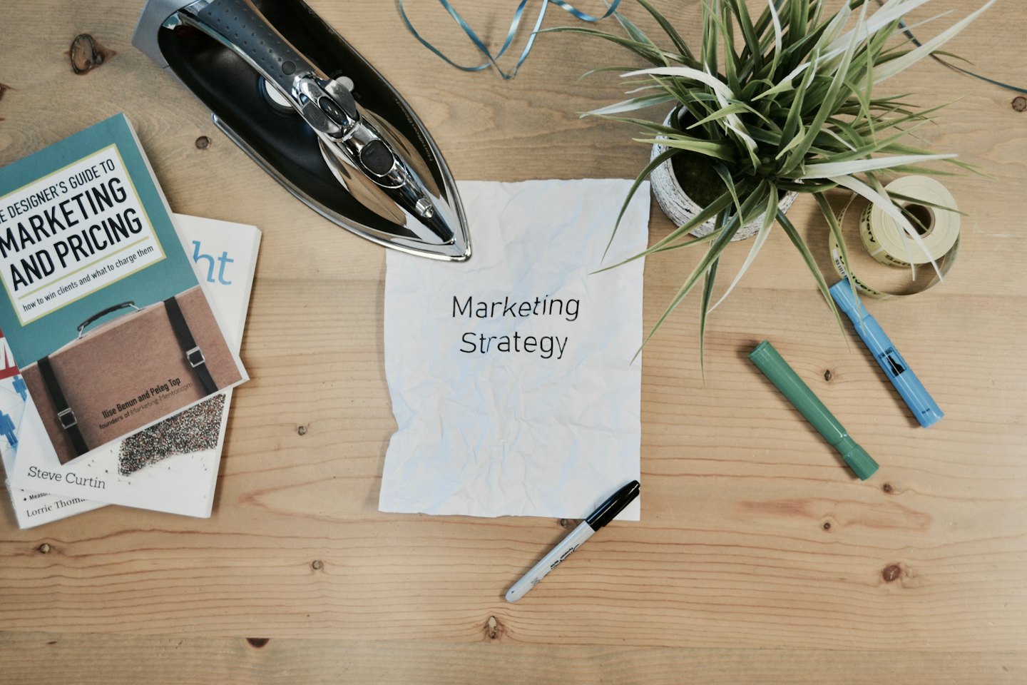 Schreibtisch aus Holz mit Marketingbüchern und zerknülltem Papier mit der Aufschrift „Marketingstrategie“.